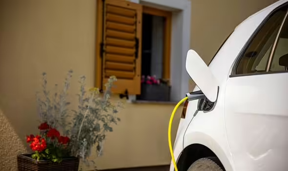 Coche eléctrico cargando en punto de recarga doméstica con energía renovable